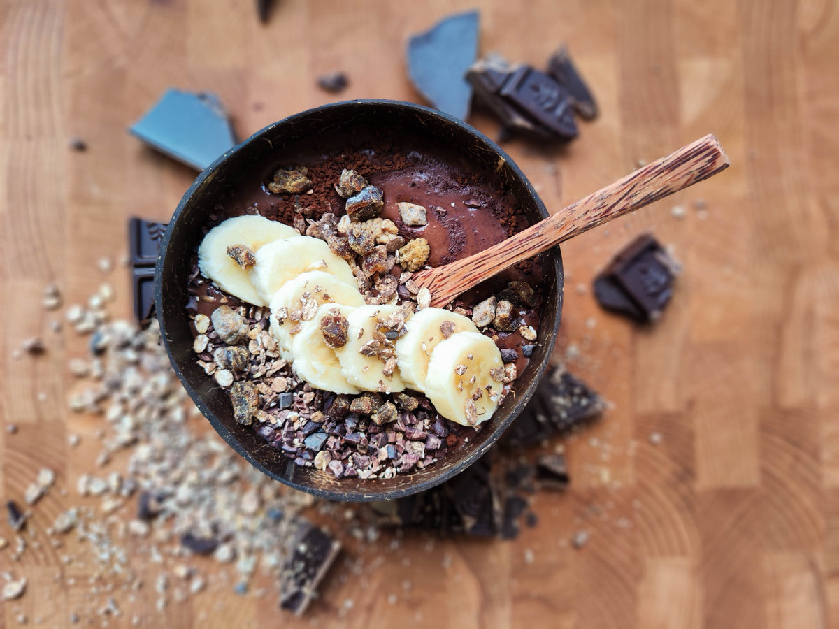 Chocolade bananen crunch bowl met chocoladebasis, plakjes banaan, cacaonibs en krokante chocoladegranola